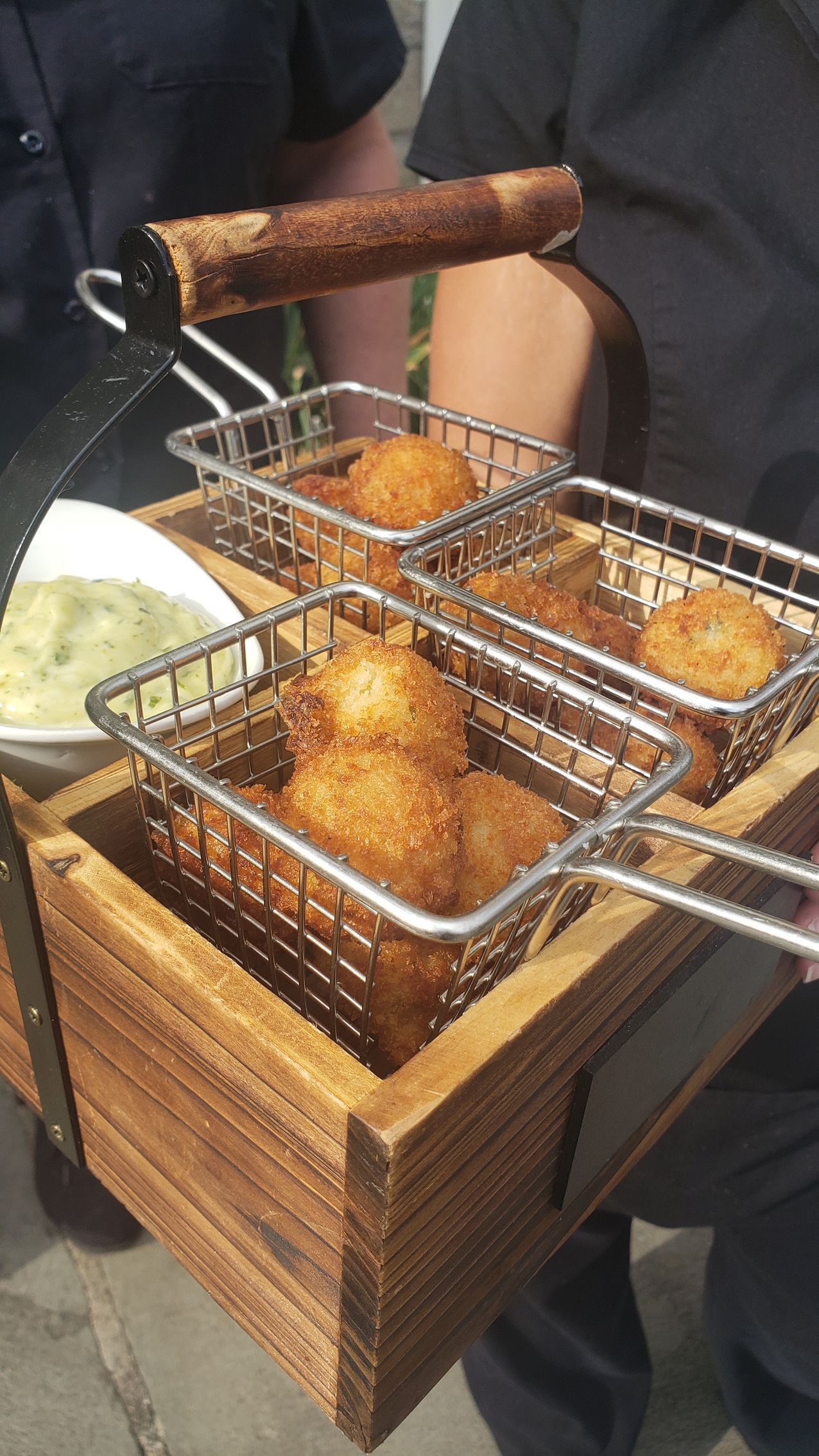 A person is holding a wooden box filled with fried food.