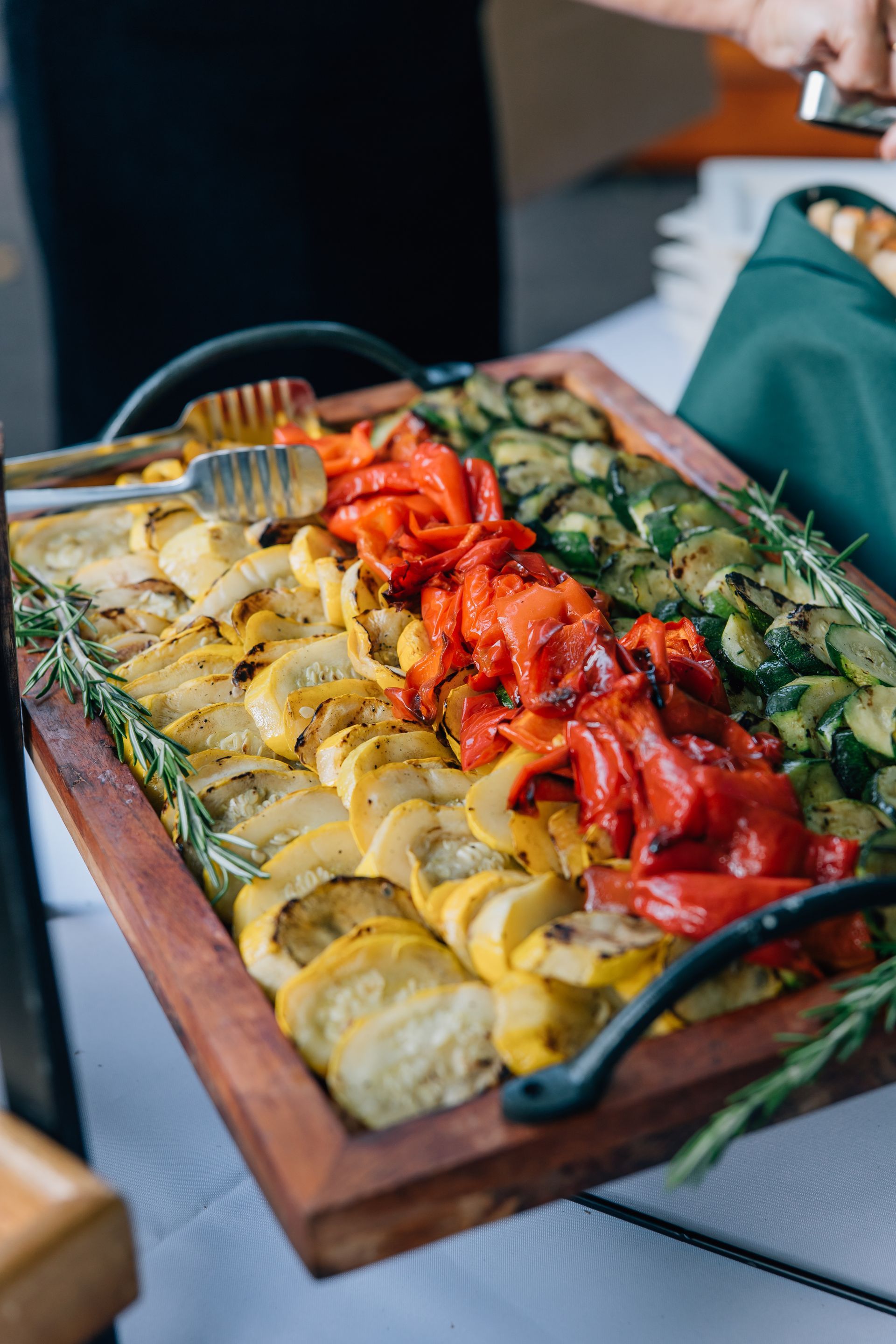 A wooden tray filled with vegetables and tongs on a table.