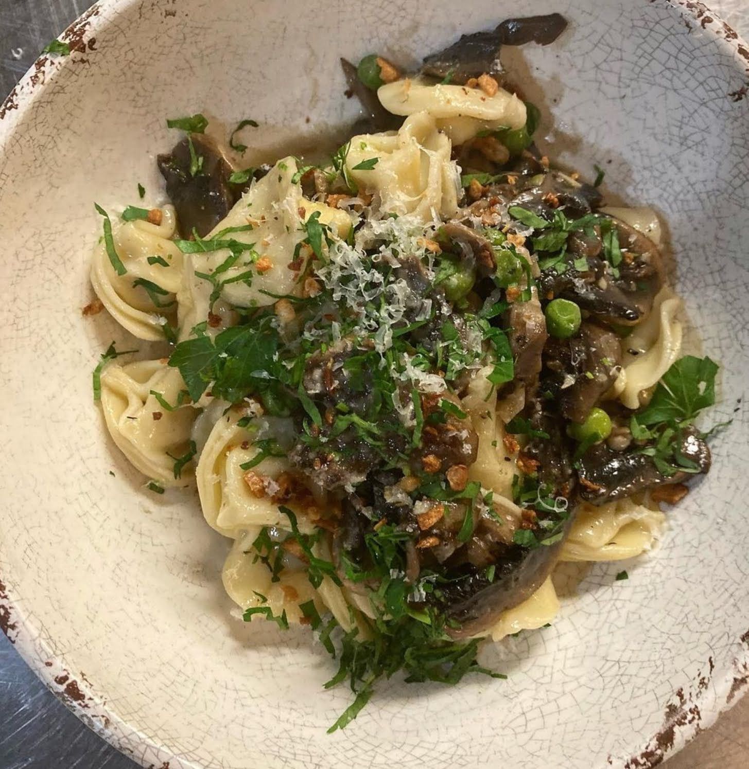 A bowl of pasta with mushrooms and peas on a table