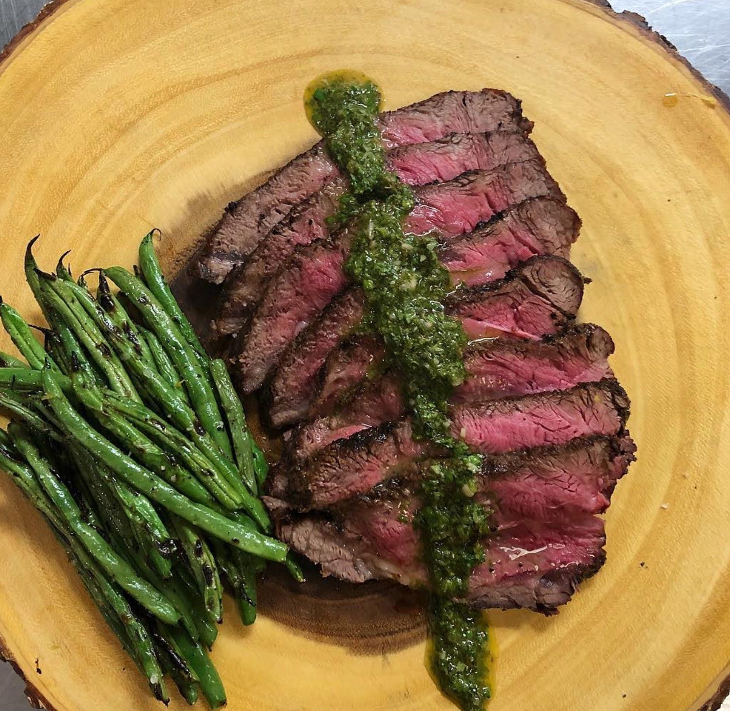 A steak and green beans on a wooden plate