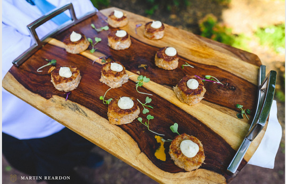 A person is holding a wooden tray with food on it.