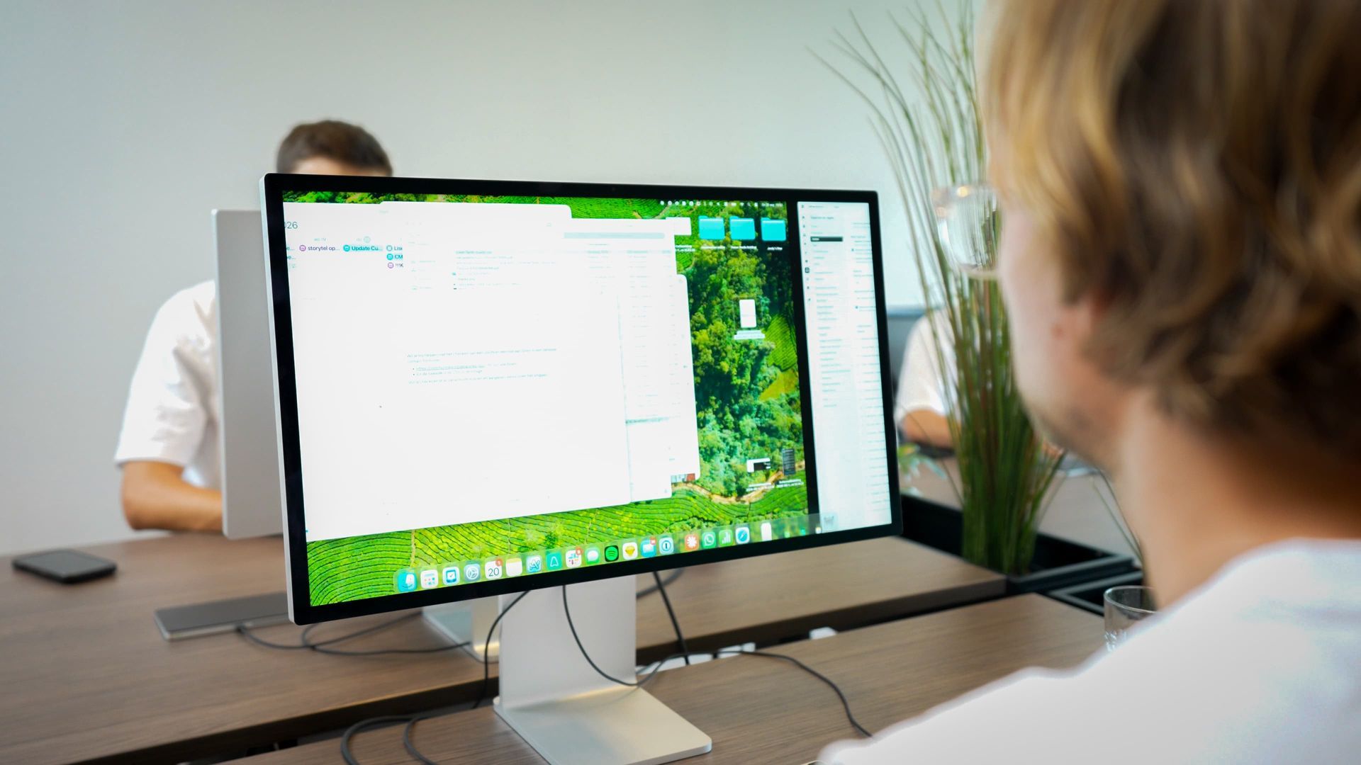 Consultant van cloudmotion achter een monitor op kantoor, met een collega op de achtergrond