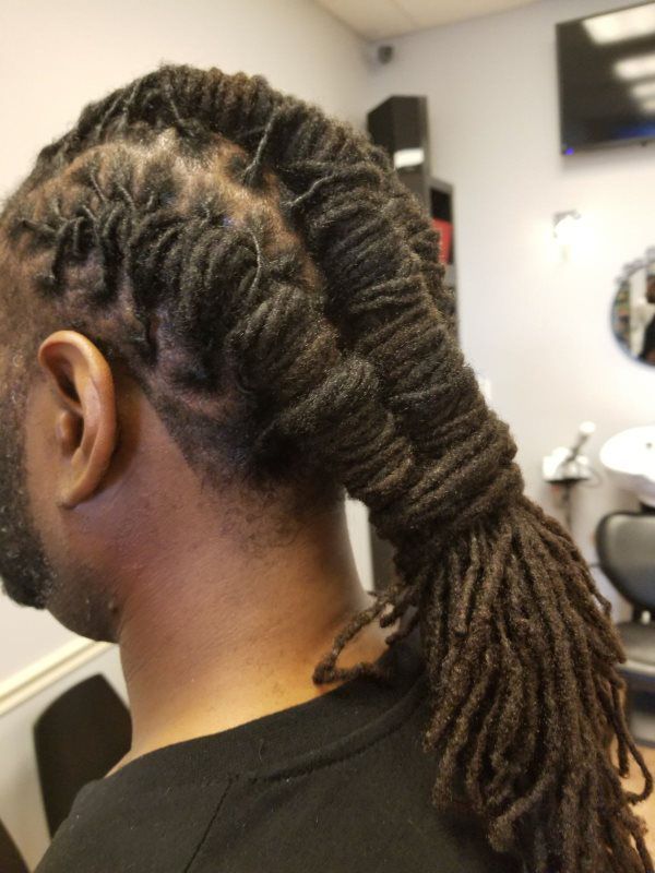 Side view of braided hair tied back in a salon chair, with a TV and mirror in the background.