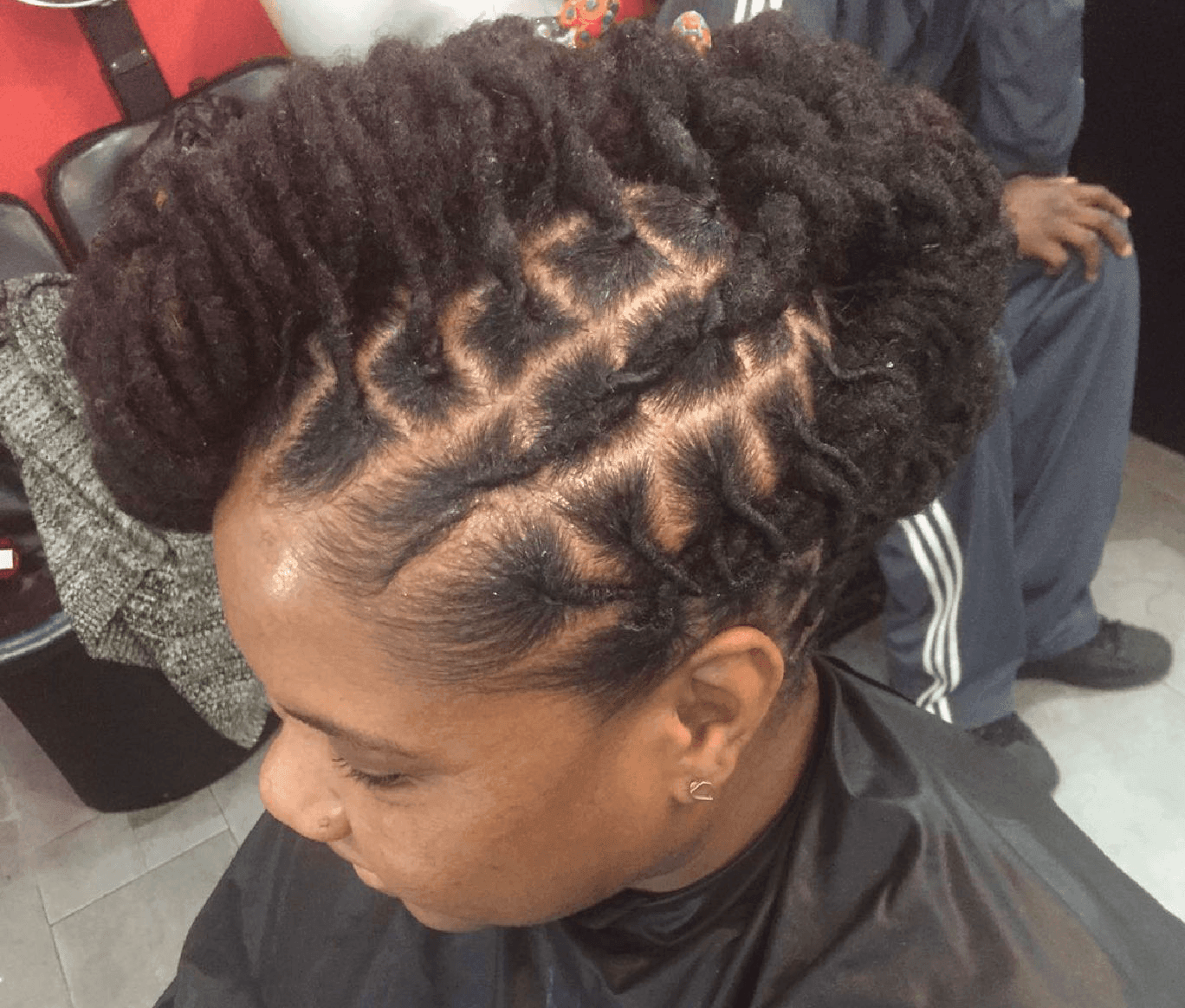 Person braiding a seated man’s hair in a dark salon chair