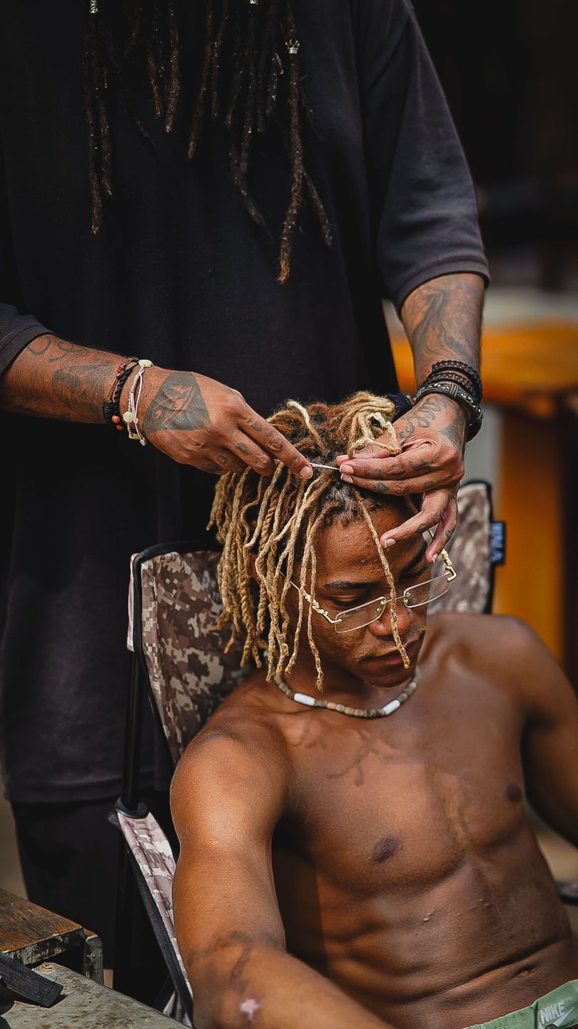 Person with dreadlocks getting hair styled while seated in a chair