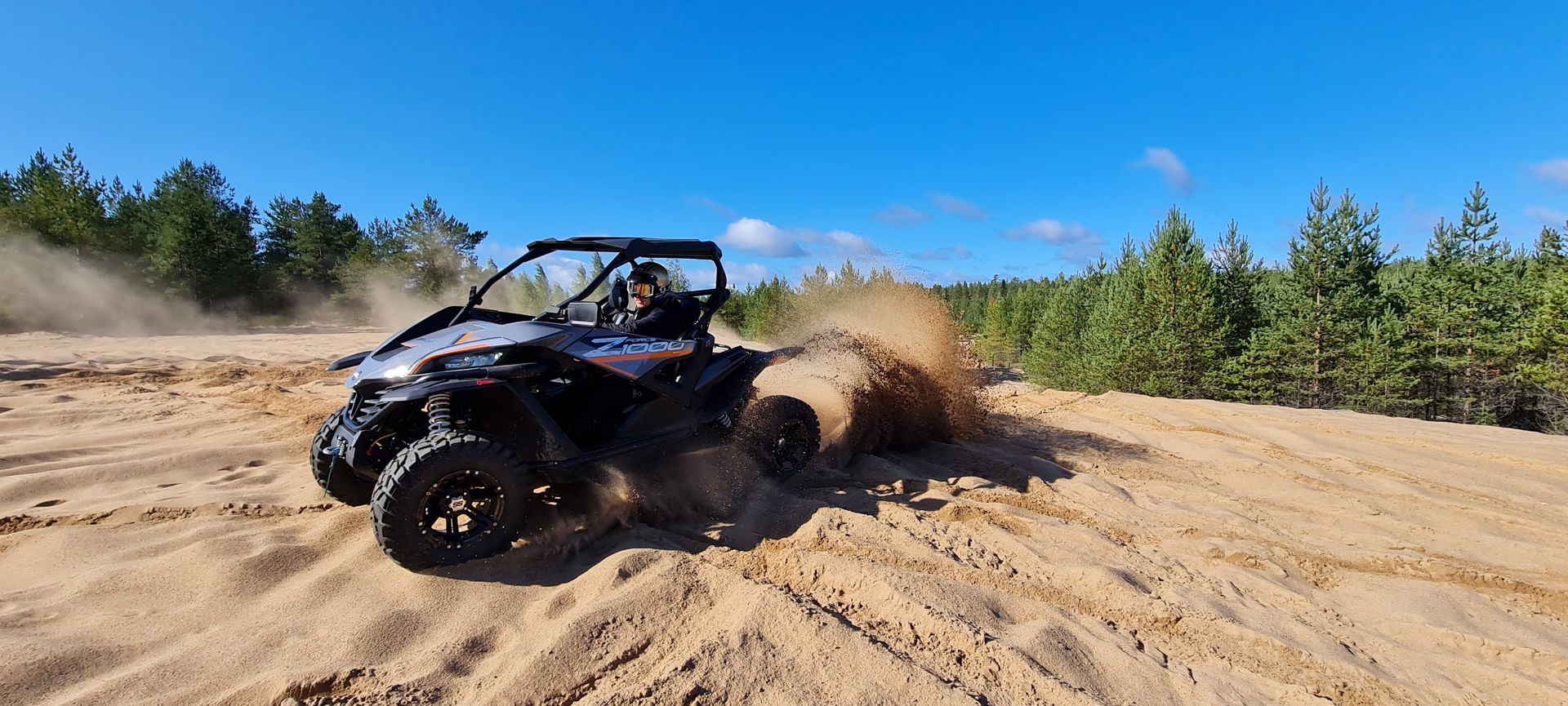 Side-by-side off-road vehicle drifting through sand, kicking up a large dust cloud in a forest clearing