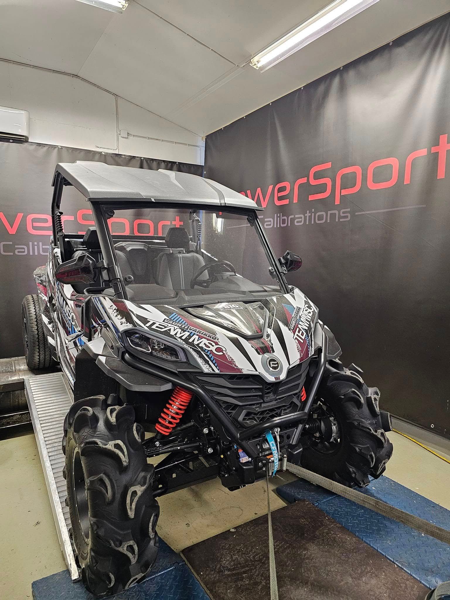 Black and silver off-road side-by-side UTV with red shocks on display indoors against a branded wall