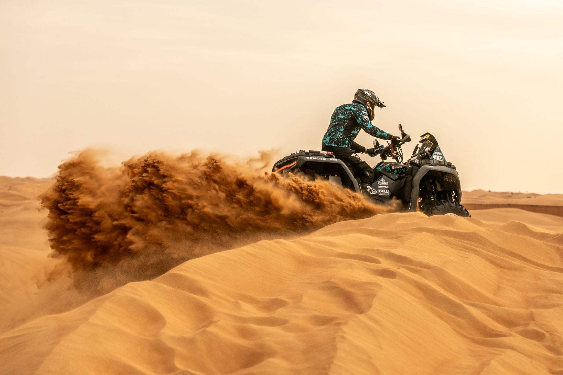 Quad bike racing across desert dunes, kicking up a cloud of sand