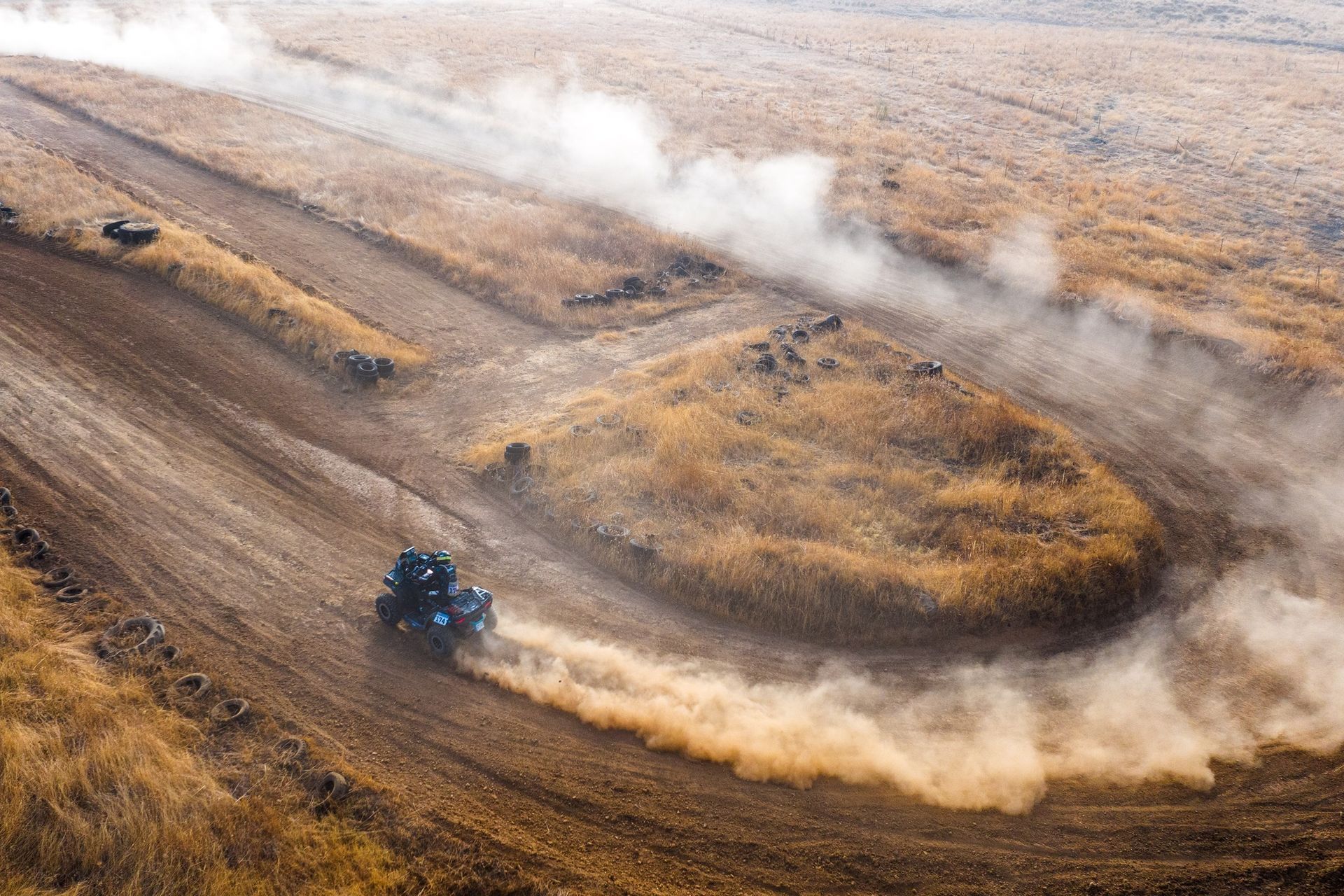 Blue rally car drifting on a dirt track, kicking up a large dust cloud around a bend