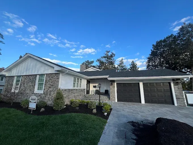 Single-story suburban house with stone exterior, garage, and landscaped front lawn under a blue sky
