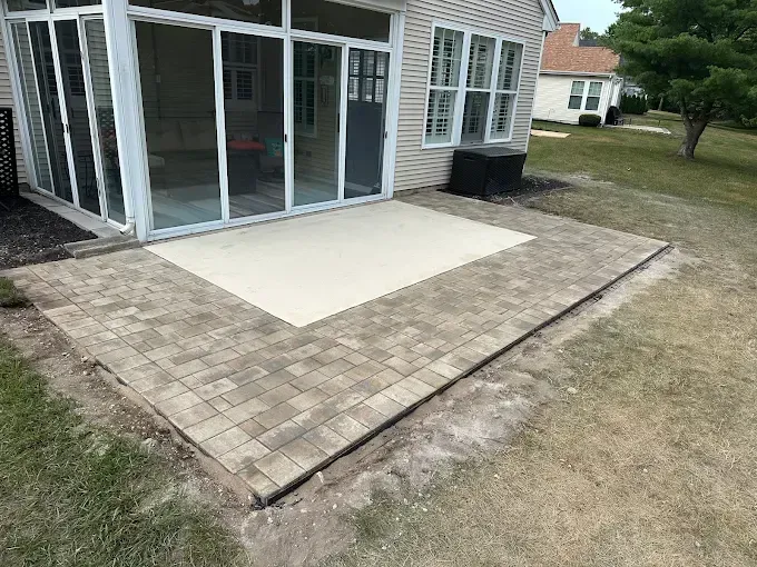 Patio with paver border and concrete slab outside a screened porch beside a grassy yard