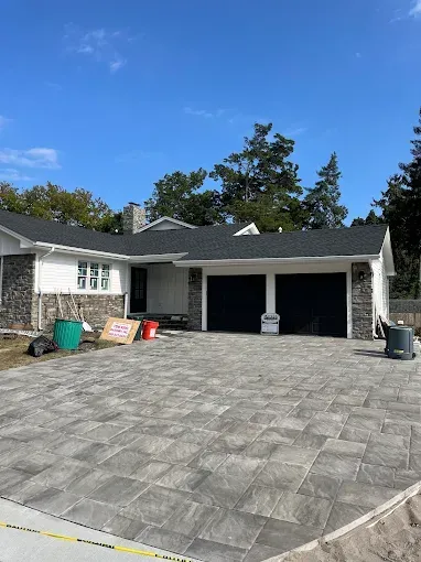 Suburban house with a wide stone driveway and two-car garage under a blue sky