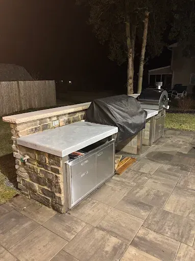 Outdoor patio with a stainless steel grill under a cover beside a stone counter at night