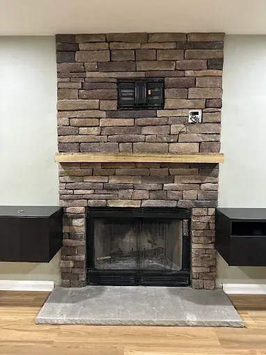 Stone fireplace with a wood mantel, black firebox, and built-in shelves on both sides