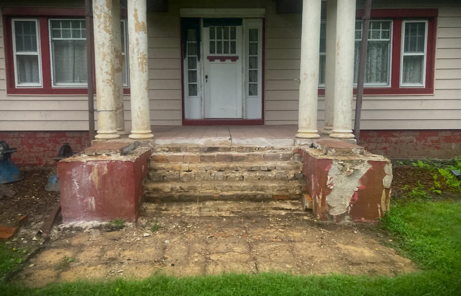 Weathered front porch with cracked concrete steps and white columns on a red house