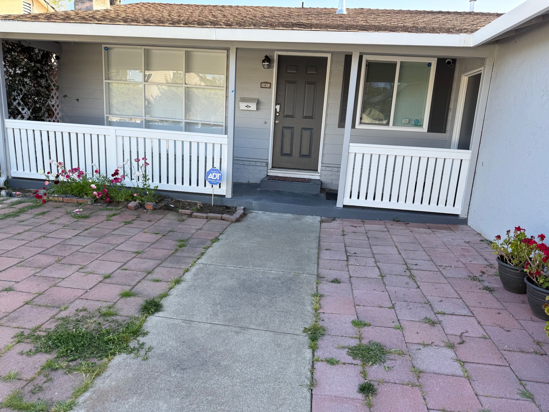 Gray house with a front porch, white railing, and a brick and concrete walkway.
