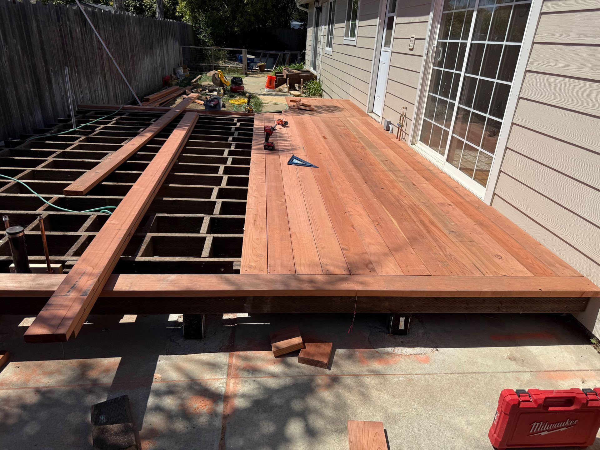 Deck construction: partially finished redwood deck with exposed framing next to a house with sliding glass doors.