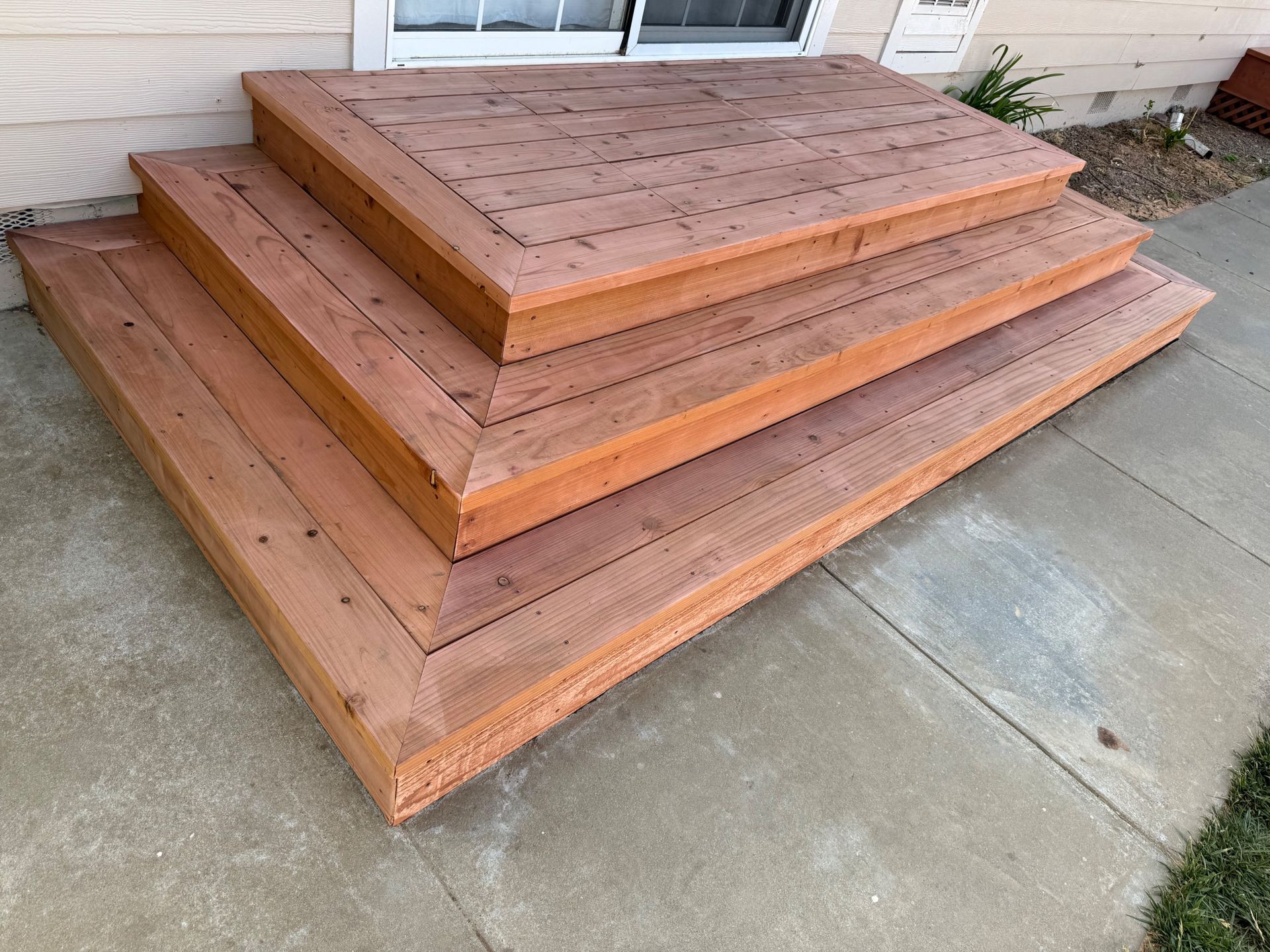 Wooden steps leading to a door, constructed on a concrete surface. Brown wood with a frame.