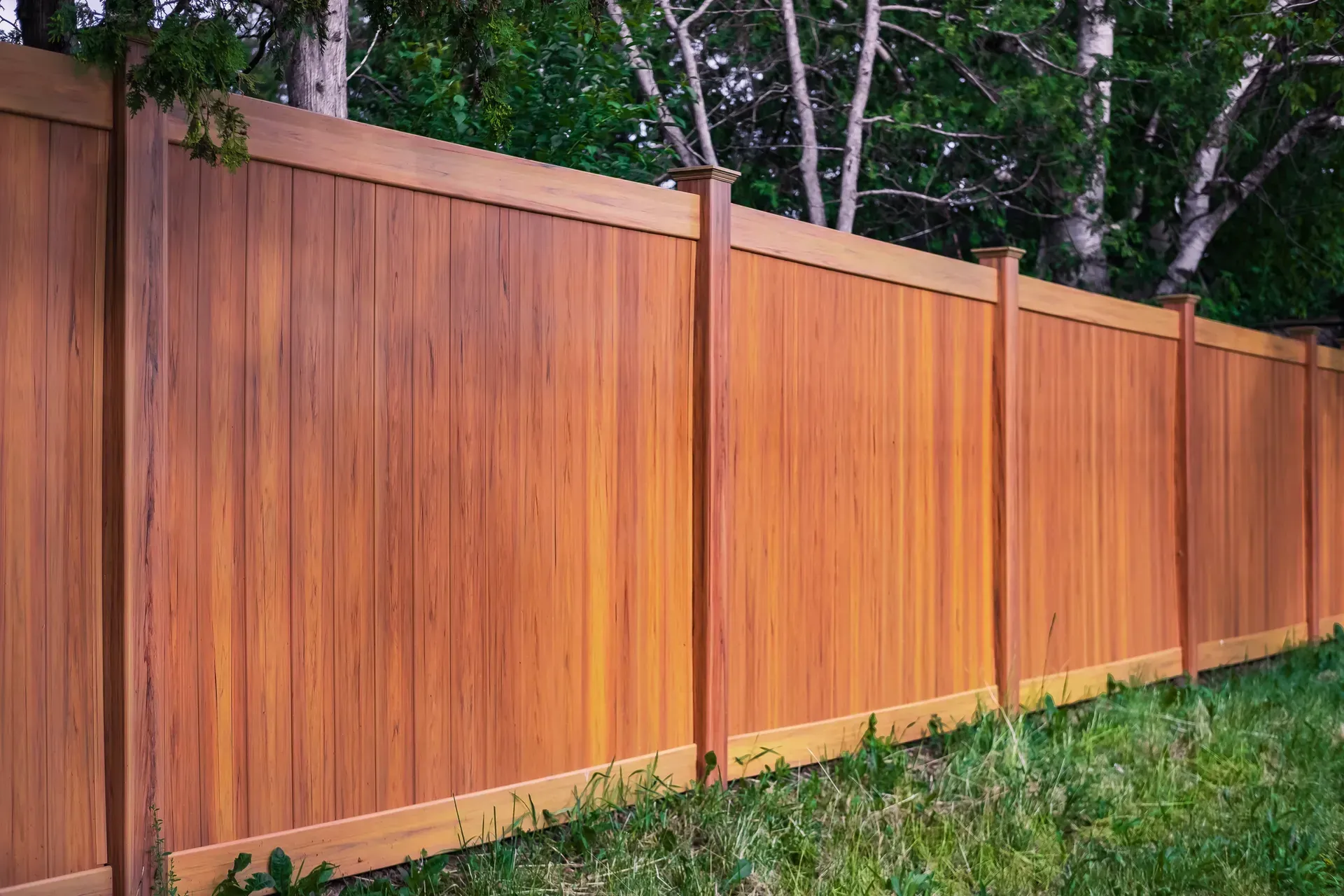 Wooden privacy fence in front of green grass and trees.