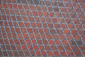 Chain-link fence in front of a red brick wall.