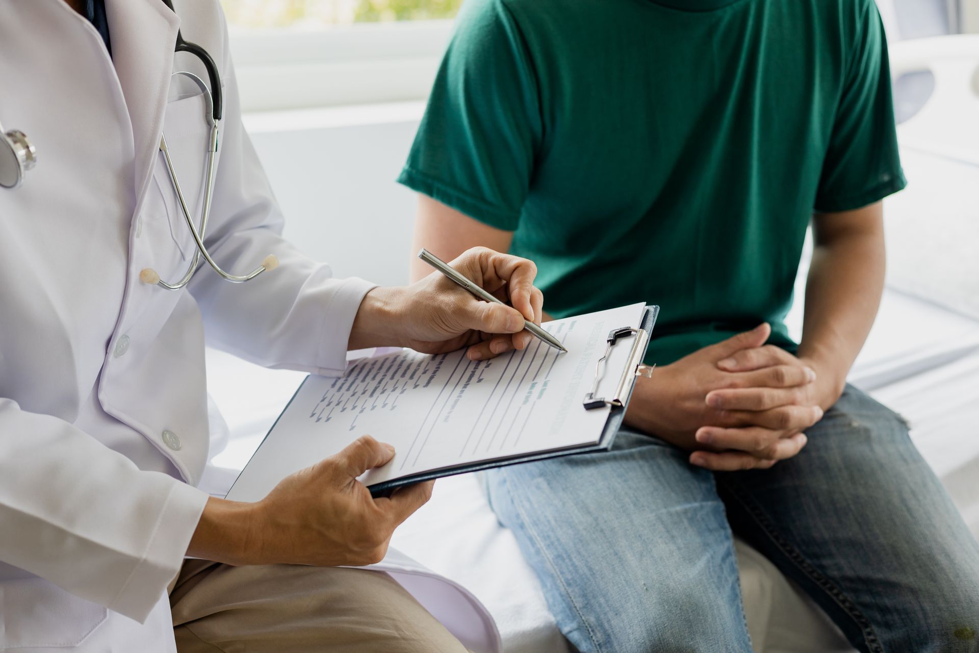 Doctor taking notes while consulting with a seated patient in a clinic