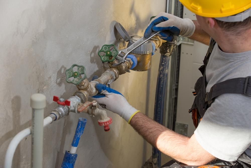 Plumber in a Yellow Hard Hat Tightening Pipes With a Wrench — ABV Plumbing In Woy Woy, NSW