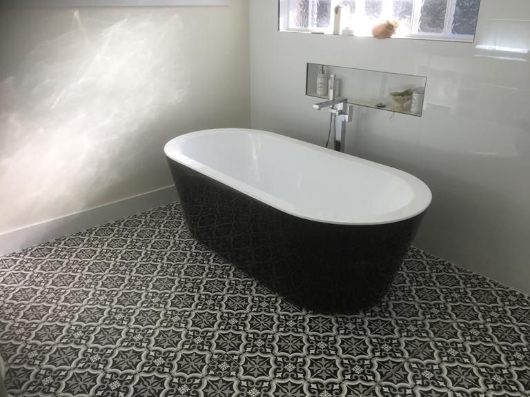 Freestanding Black and White Bathtub in a Bathroom With Patterned Tile Floor — ABV Plumbing In Woy Woy, NSW