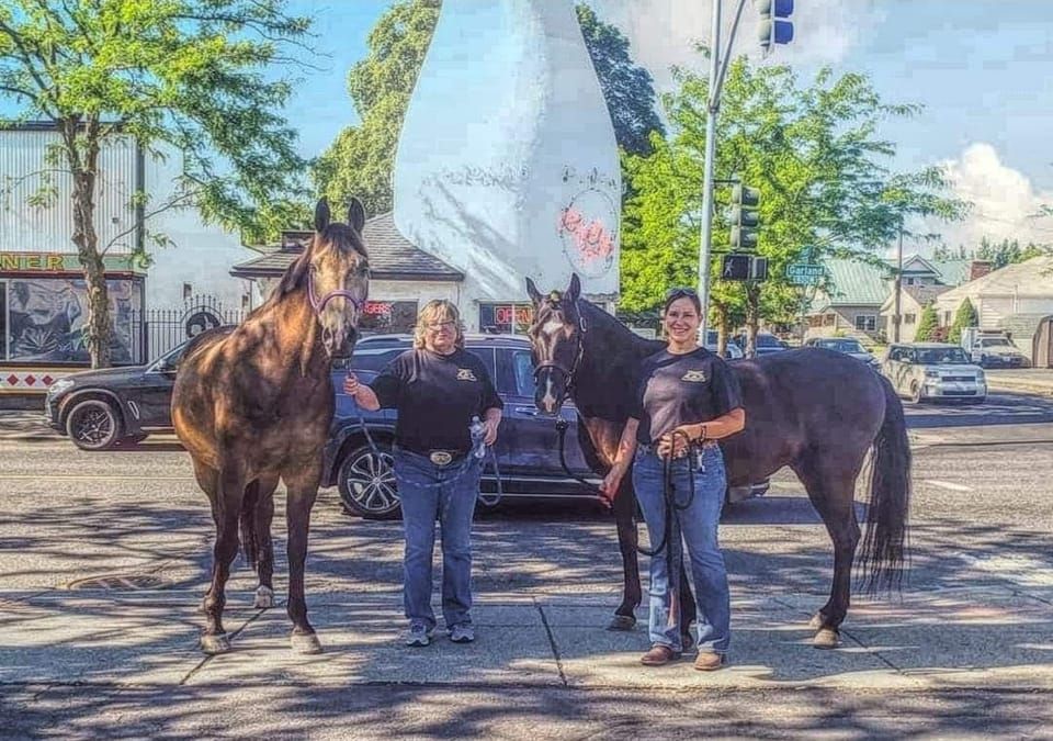Two women are standing next to two horses in front of the Milk Bottle in Spokane