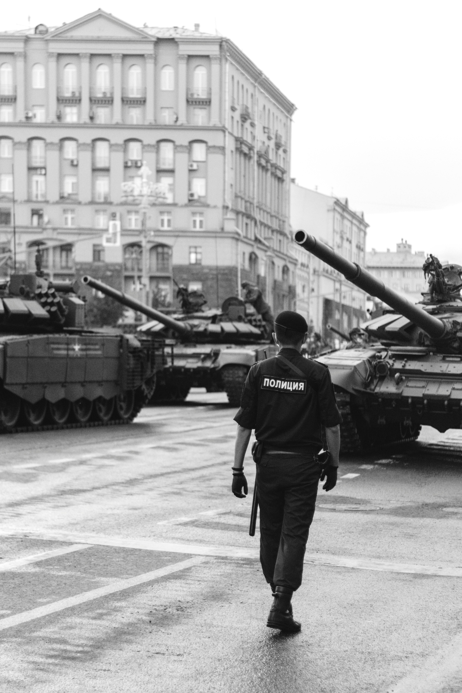A black and white photo of a man walking in front of a row of tanks