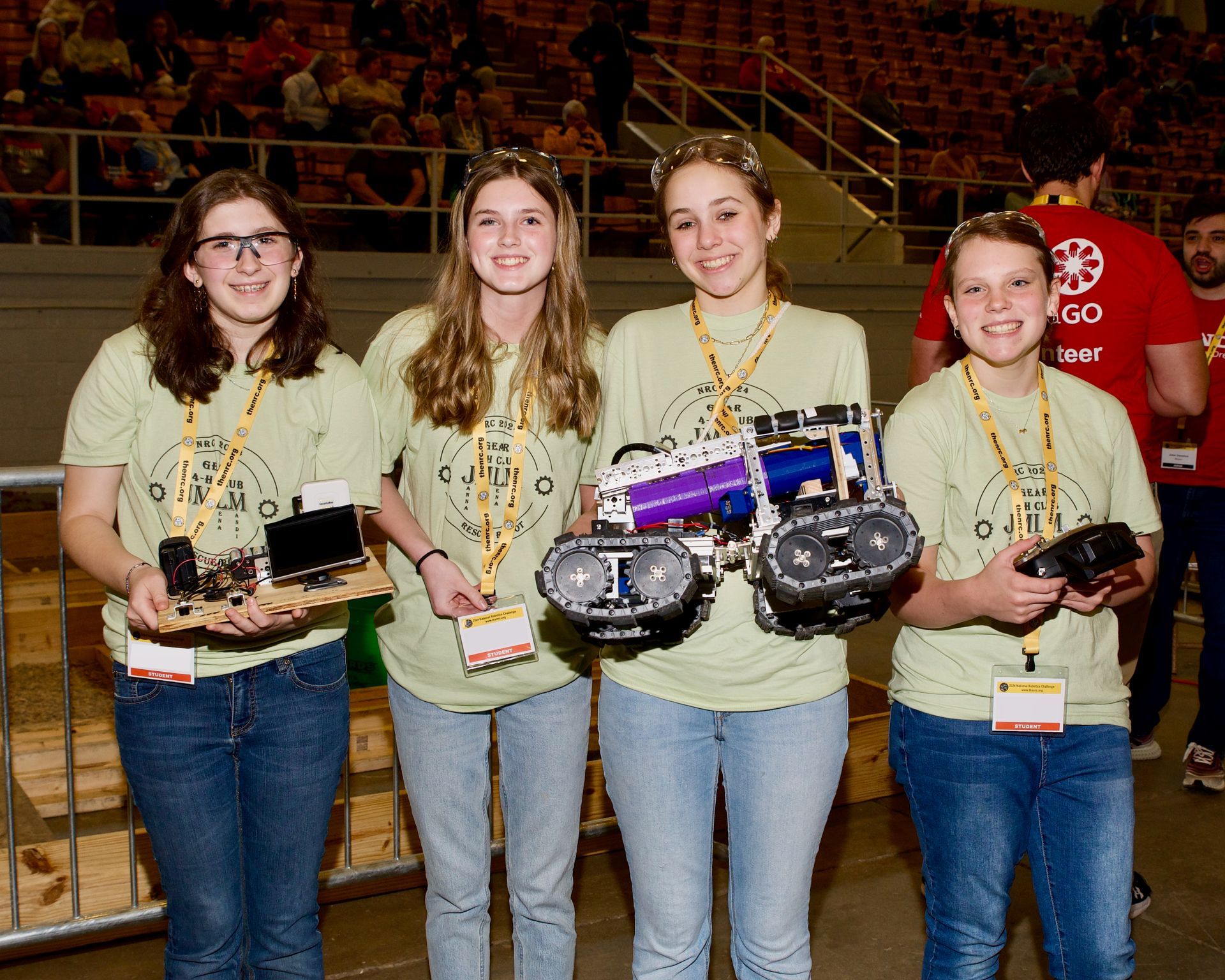 A group of girls are holding their robots in front of a crowd