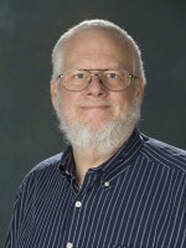 A man with a beard and glasses is wearing a blue striped shirt.