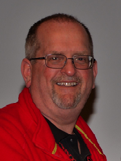 A man wearing glasses and a red jacket smiles for the camera
