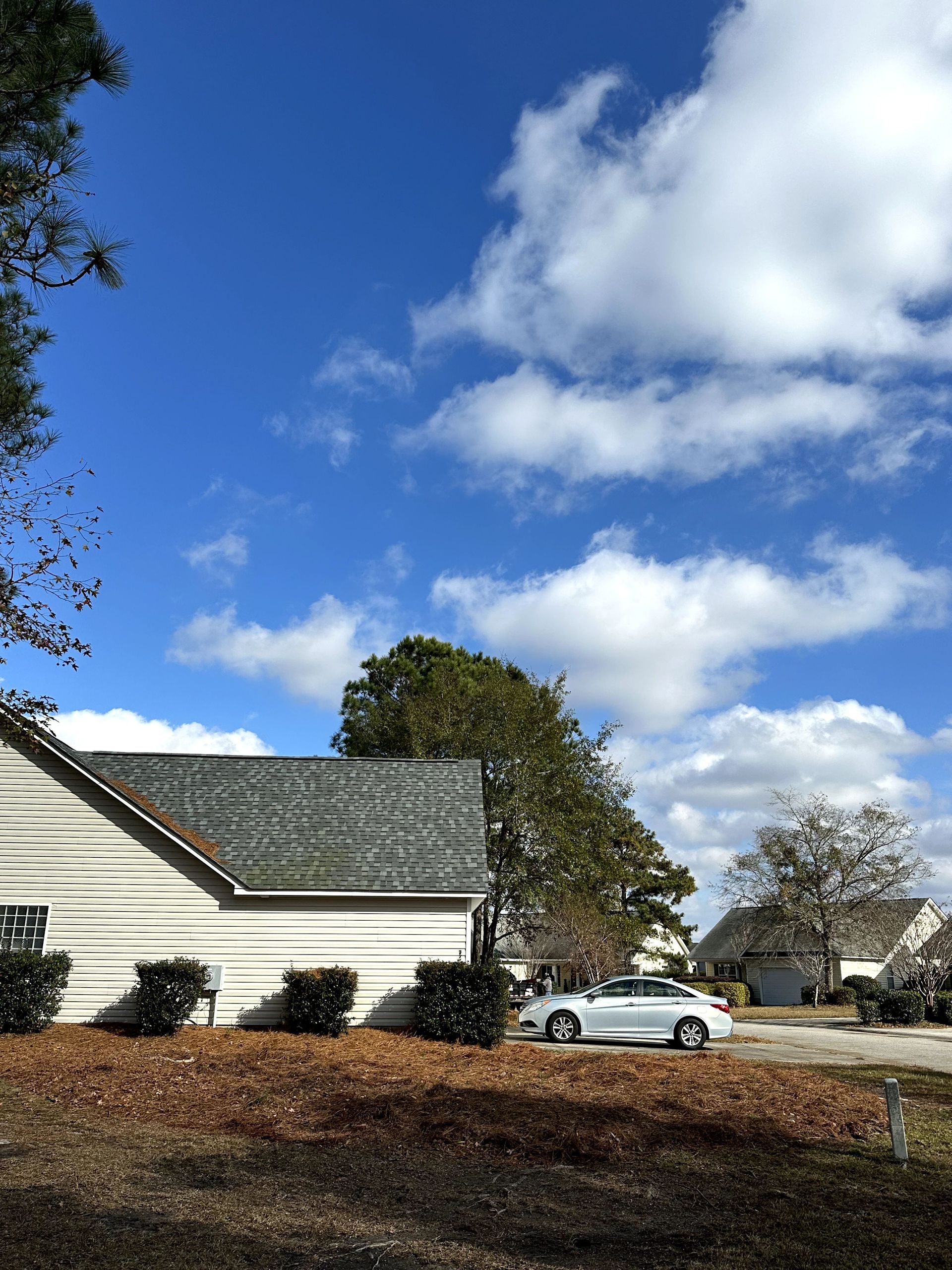 White house with gray roof and a silver car under a bright blue sky with clouds