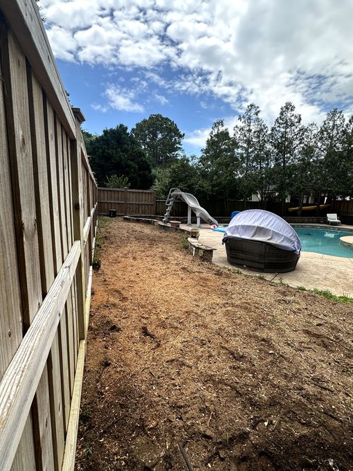 Backyard with wood chip ground, wooden fence, pool, and playground slide under a partly cloudy sky