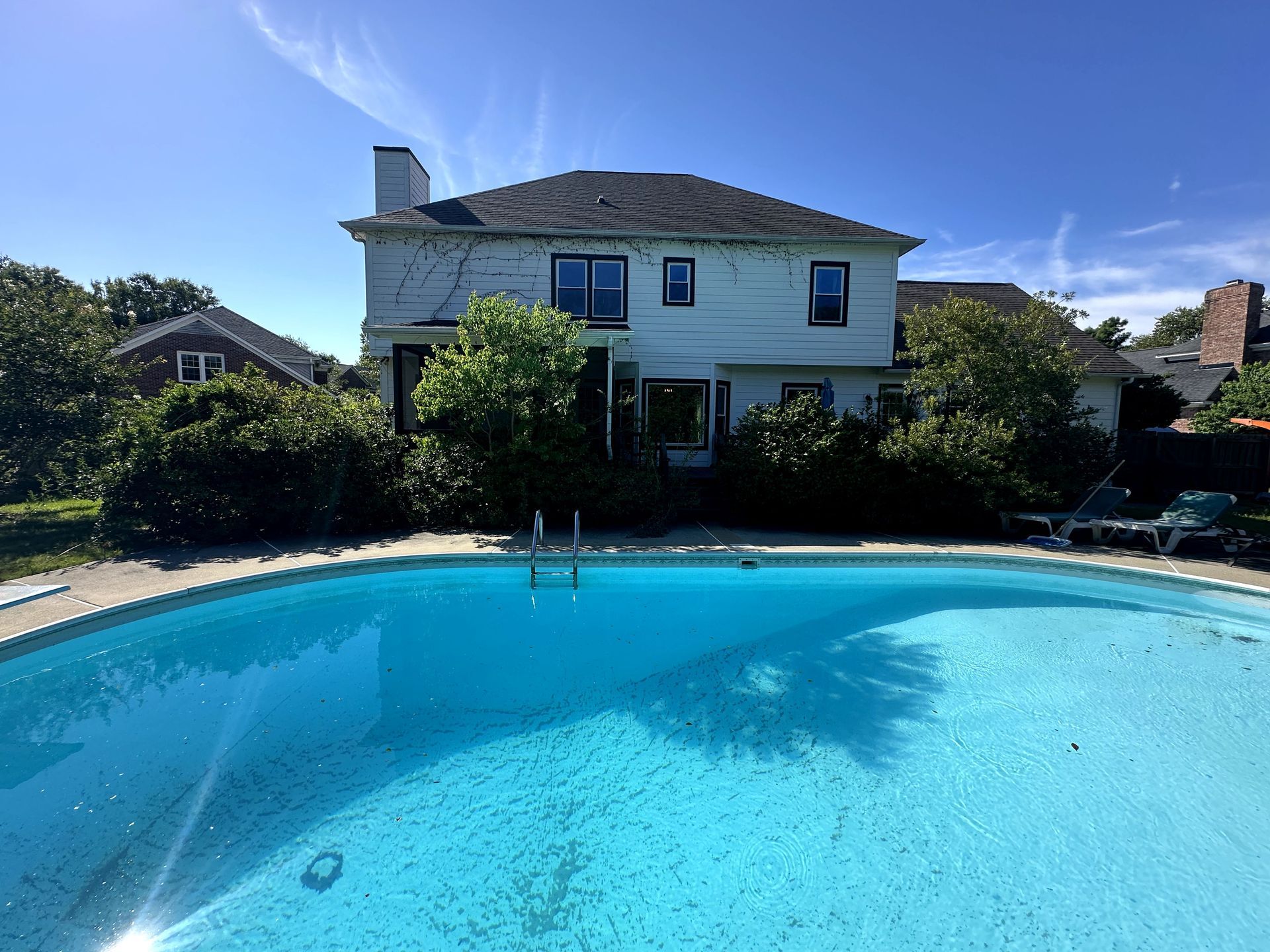 Backyard pool in front of a two-story white house on a sunny day