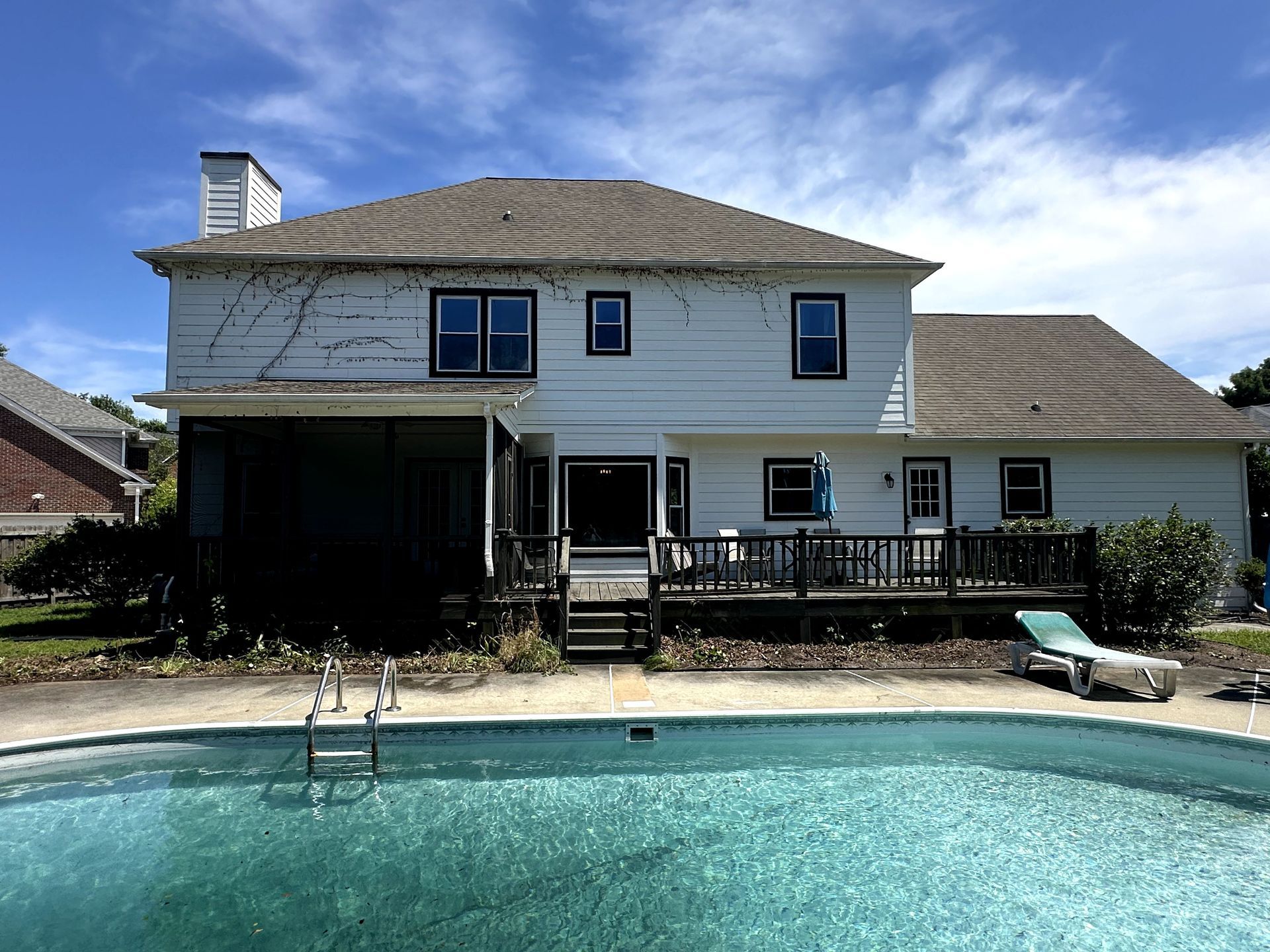 Two-story house with a backyard swimming pool and wooden deck in bright sunlight