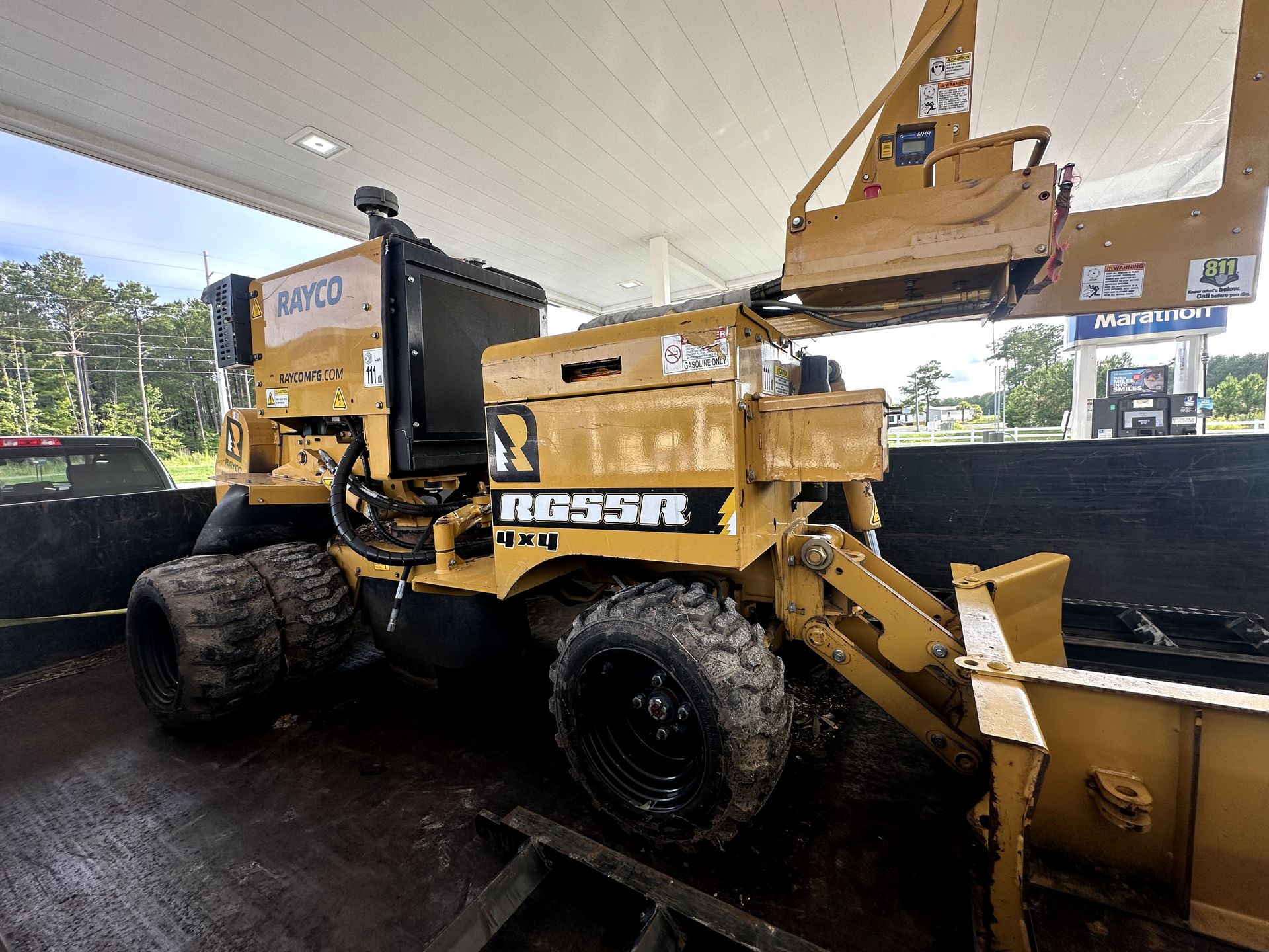 Yellow road roller at a construction site, lifting asphalt under a canopy with a bucket loader nearby
