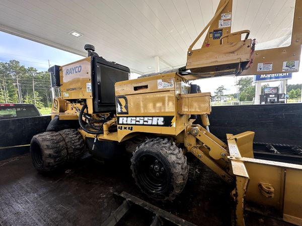 Yellow road roller at a construction site, lifting asphalt under a canopy with a bucket loader nearby