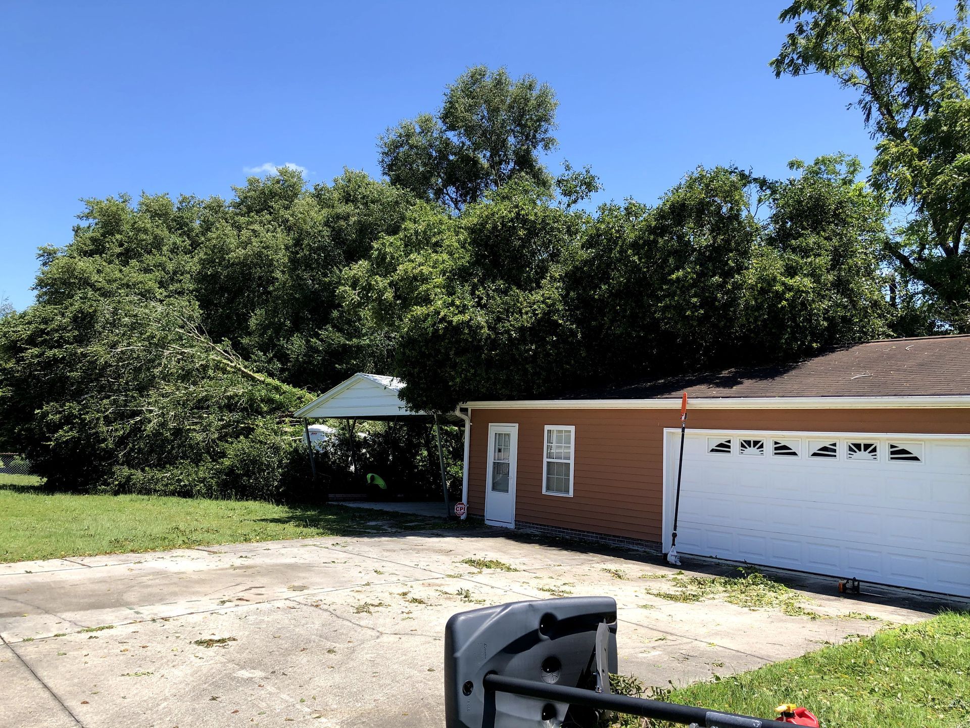 Suburban driveway beside a brick garage and trees under a clear blue sky