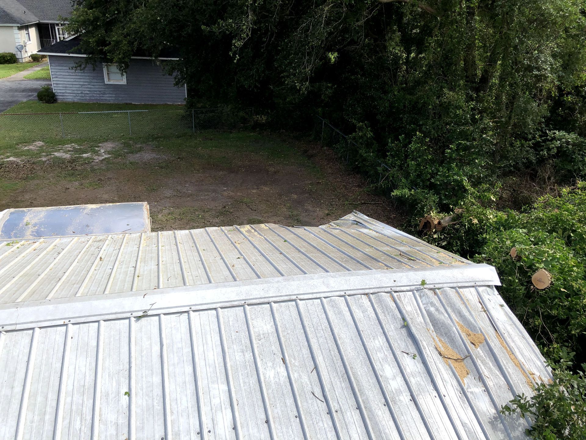 Weathered rooftop deck overlooking a dirt yard and dense green trees beside a house.
