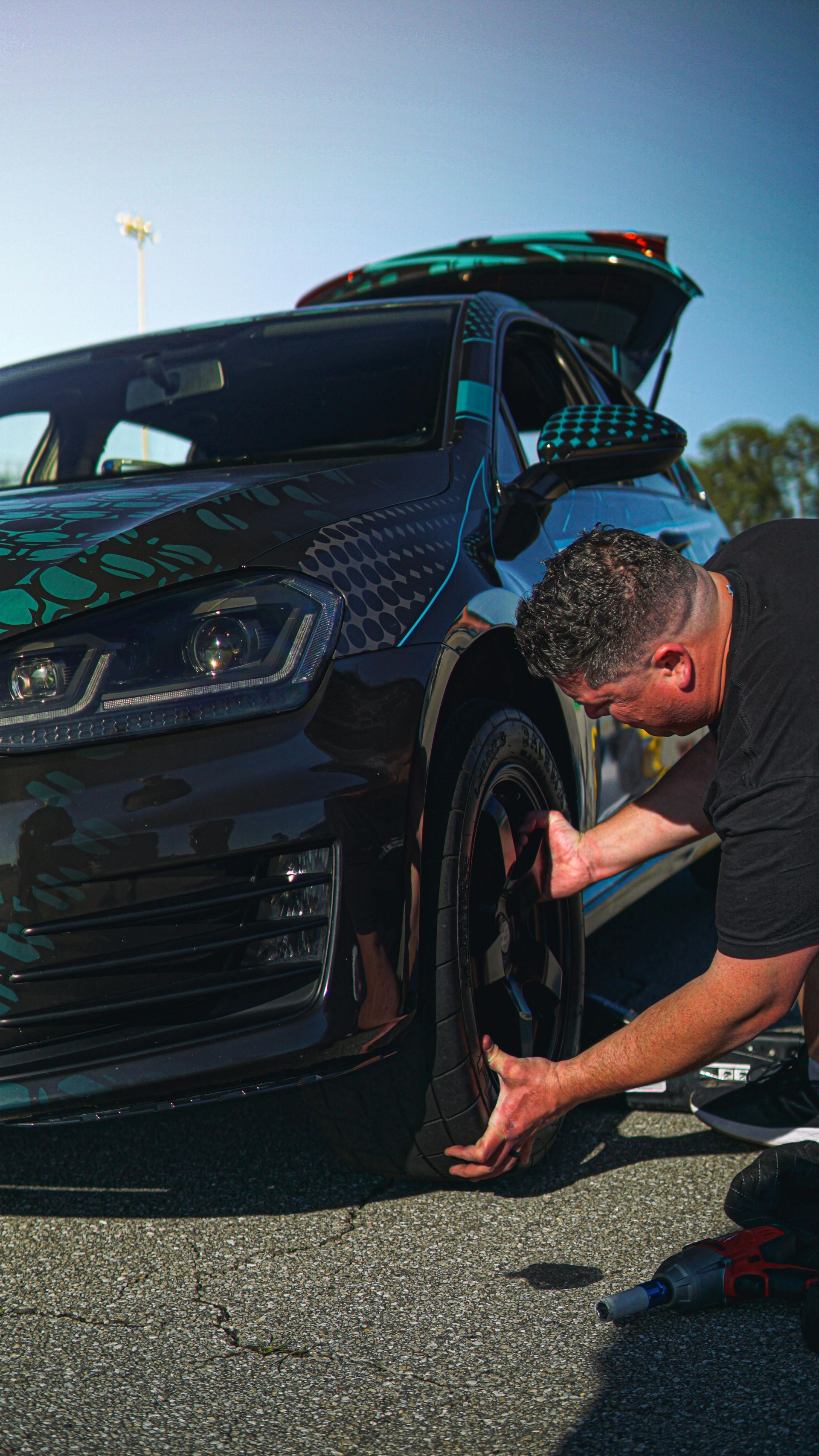 A man is changing a tire on a black car.