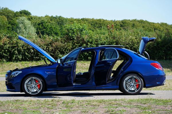 A blue car with the hood up is parked in a field.