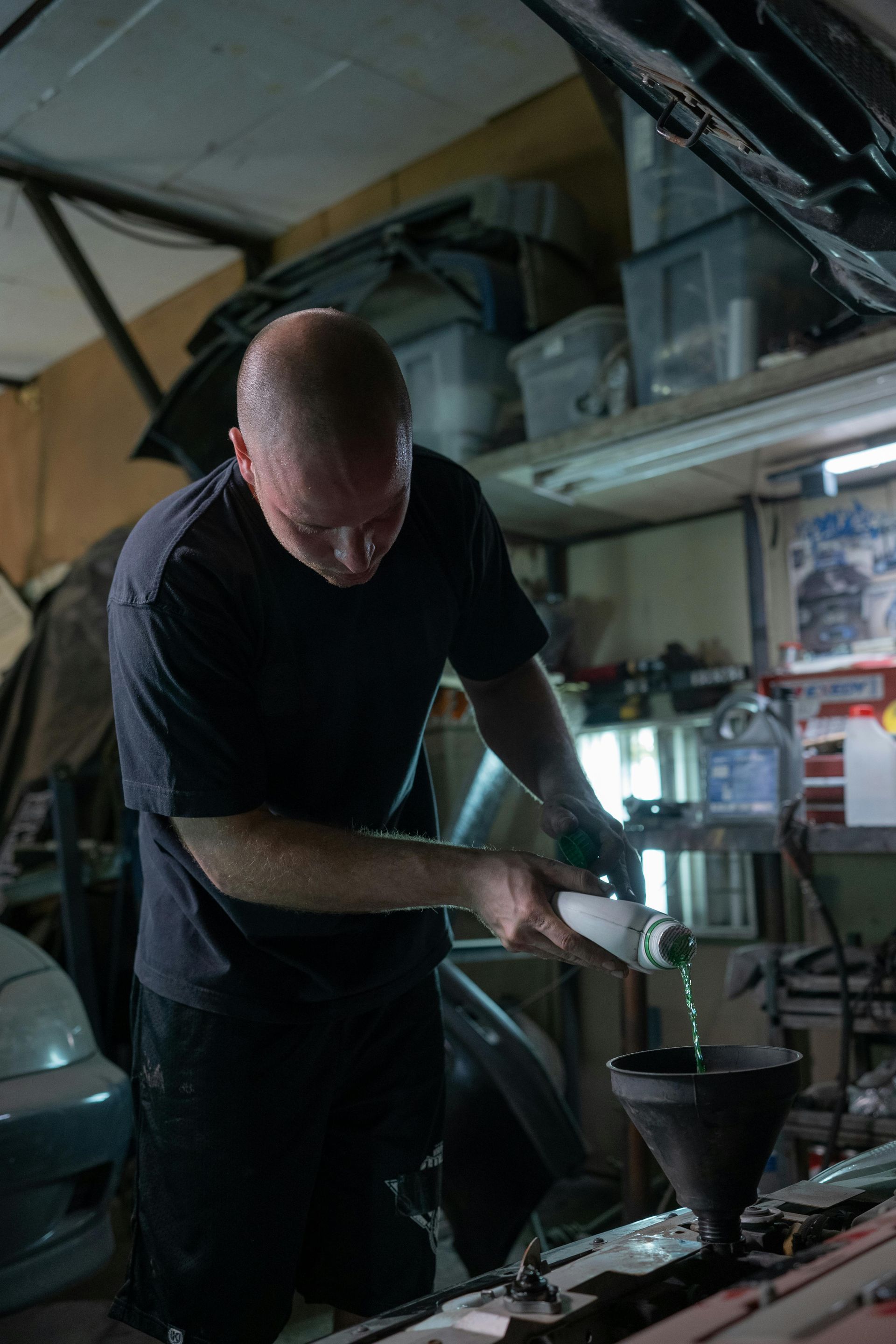 A man is pouring oil into a funnel from a bottle.