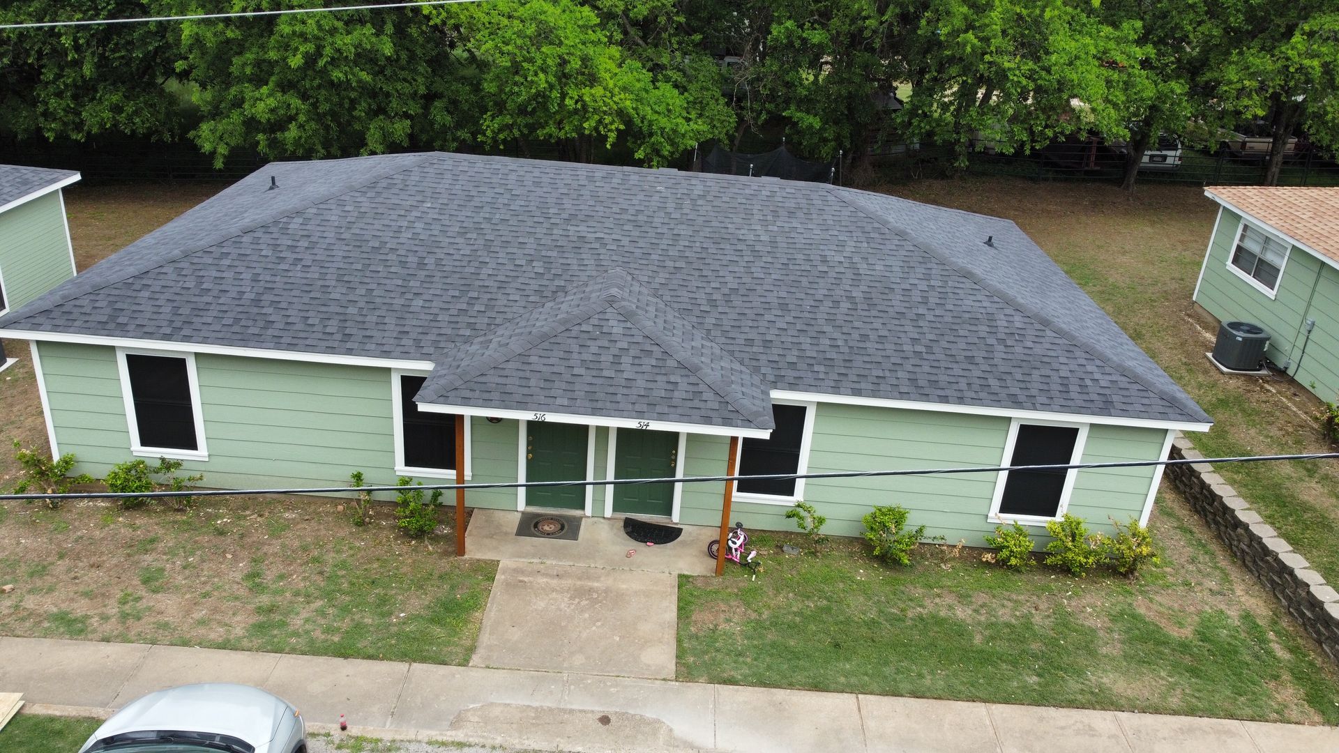 An aerial view of a green house with a car parked in front of it.