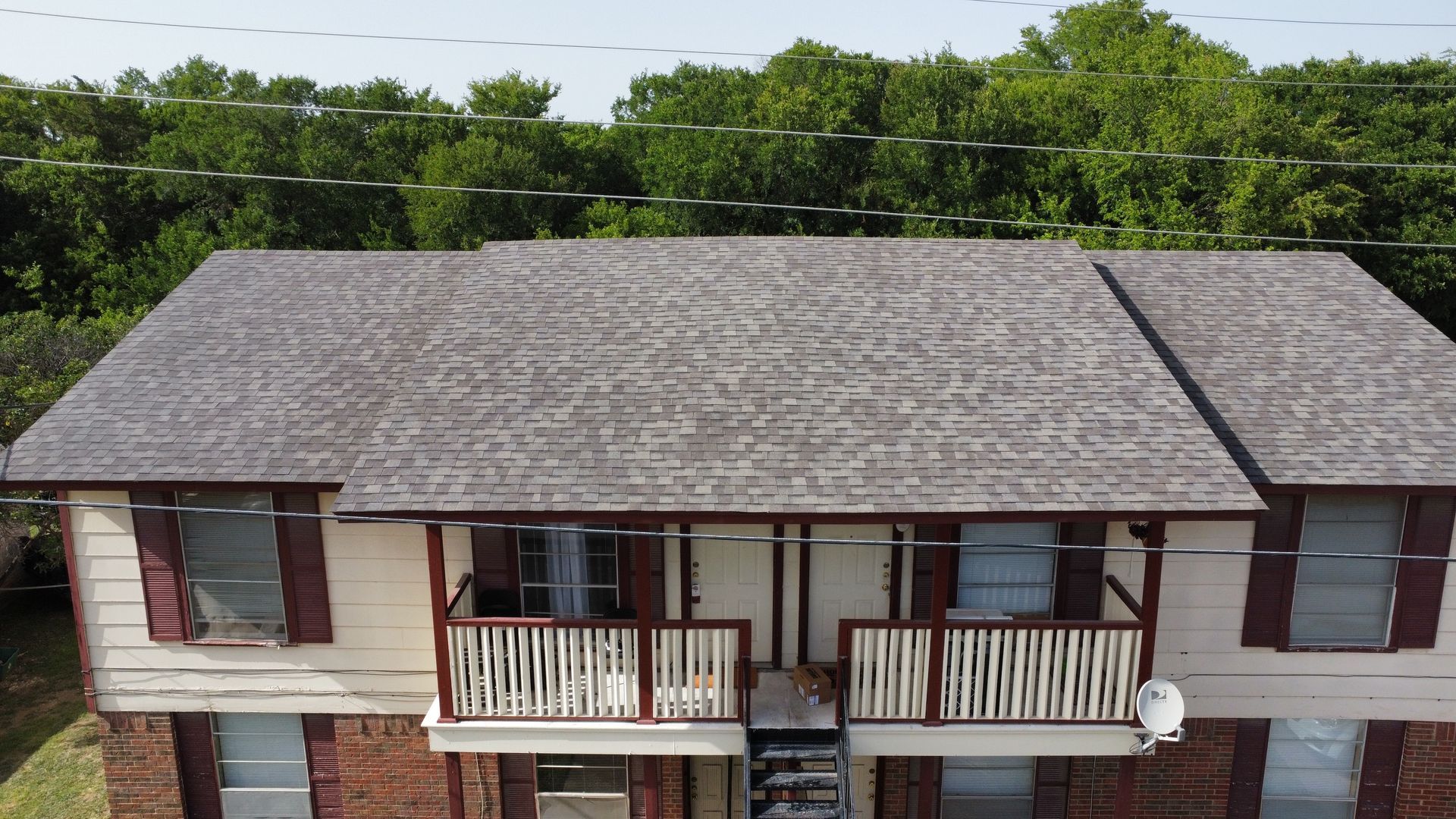 An aerial view of a brick apartment building with a roof that is covered in shingles.