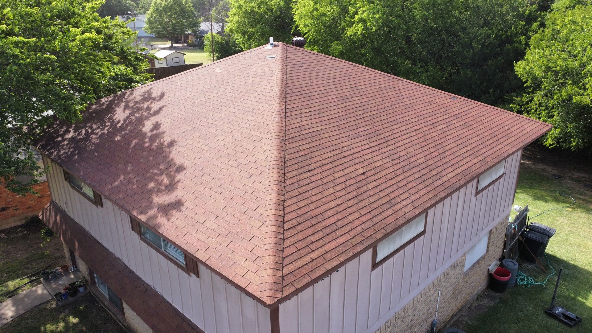 An aerial view of a house with a brown roof surrounded by trees.