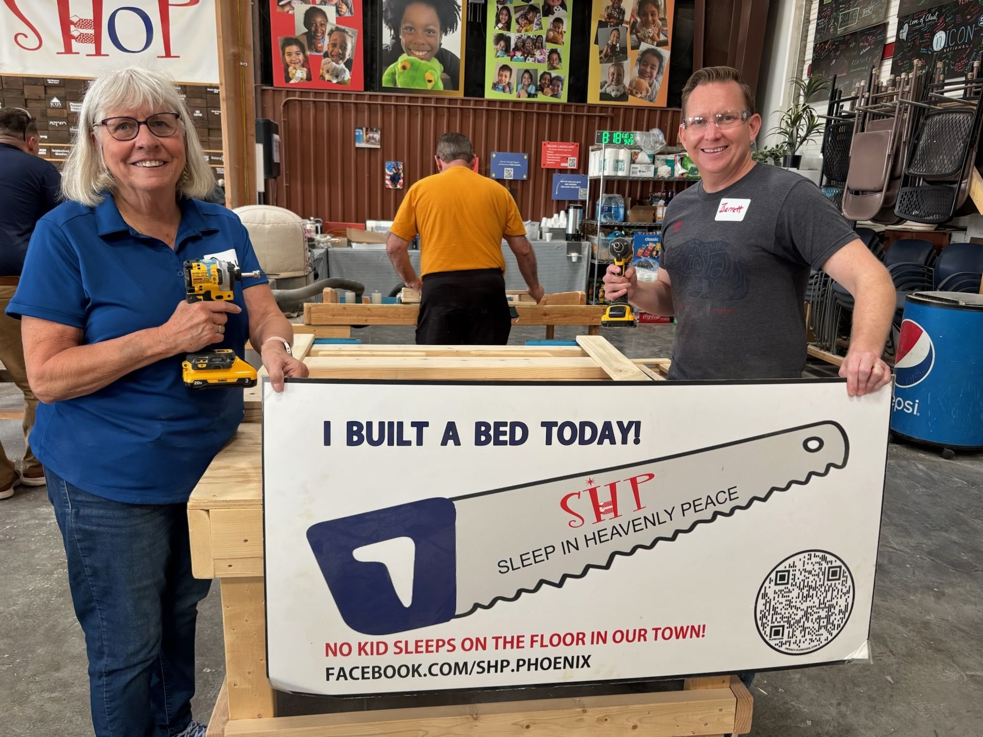 Volunteers holding drills and an I Built a Bed Today sign