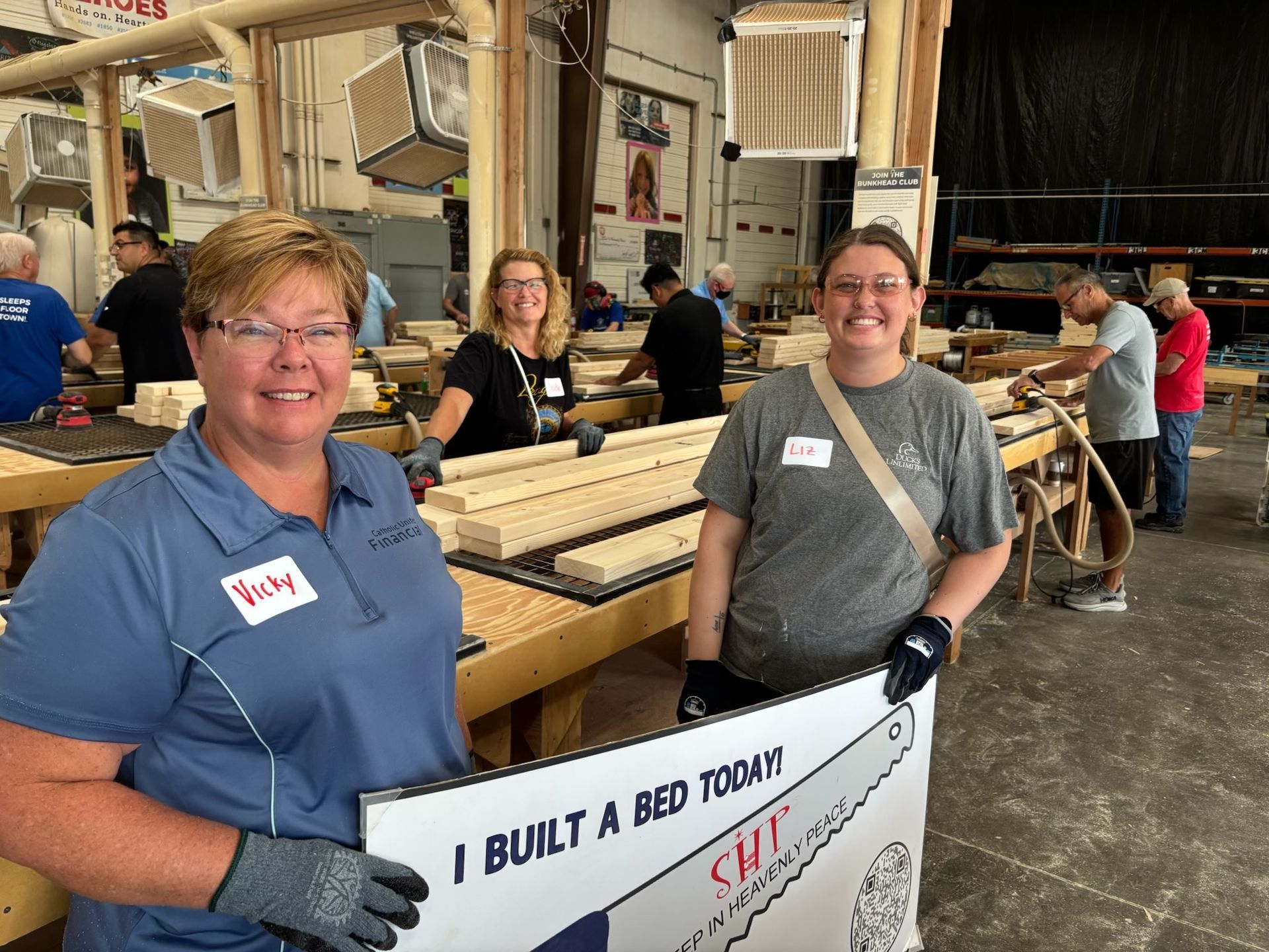 Two volunteers beside wooden bed components in the SHP workshop