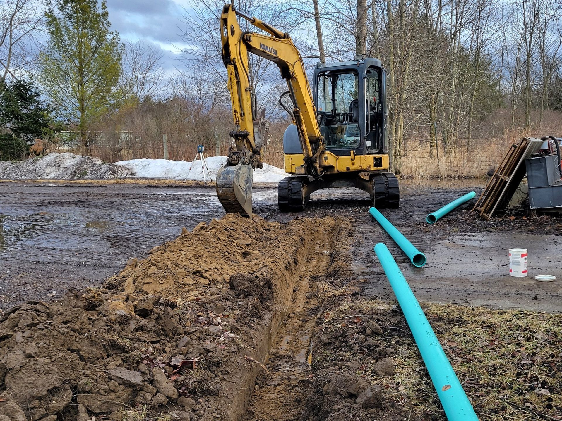 Yellow excavator digging by blue pipes at a muddy construction site