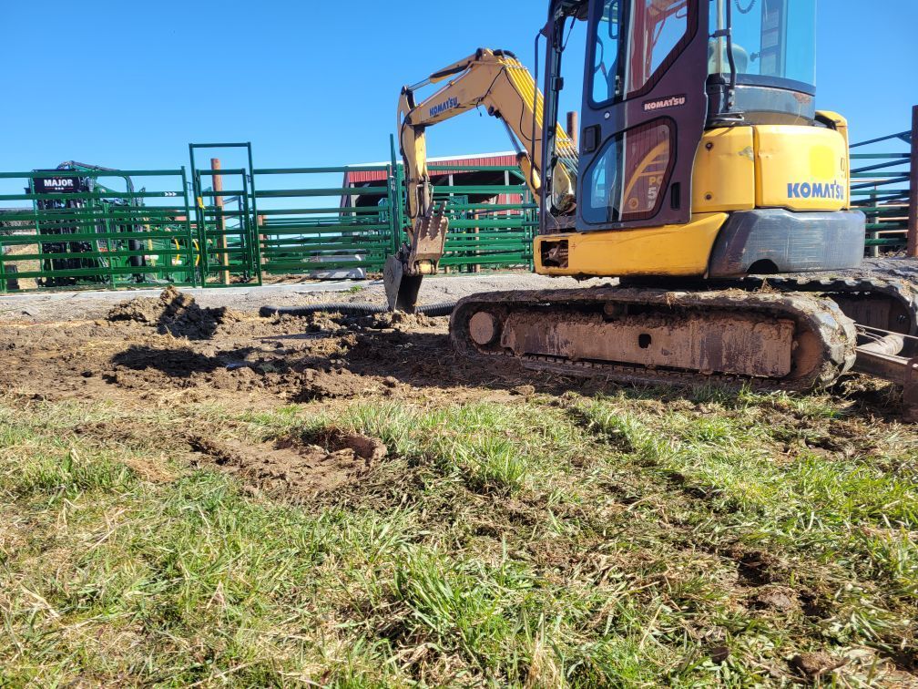 Yellow excavator digging dirt beside a green fence in a muddy field.